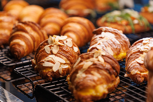 Close-up on beautifully baked crusty croissant on a grid in cafeteria, filled with cream, chocolate topping and almond flakes