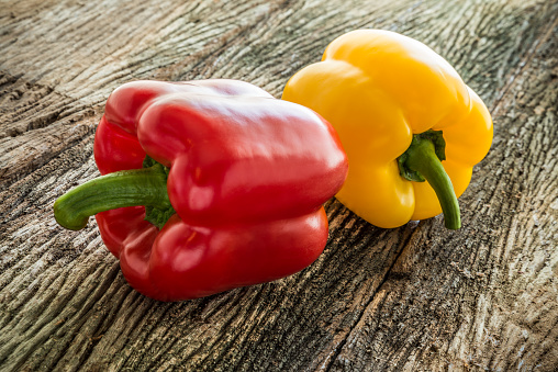 Red and yellow sweet or bell pepper on old wooden background. Food material, fruit, diet concept.