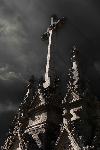 Stone cross on old stone church, stormy skies, dark and mysterious, light shining thru clouds