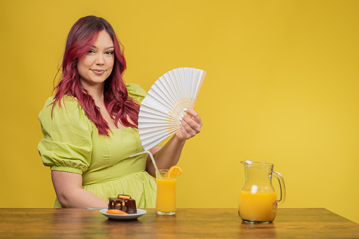 young beautiful chubby redhead girl drinking juice in studio on yellow background