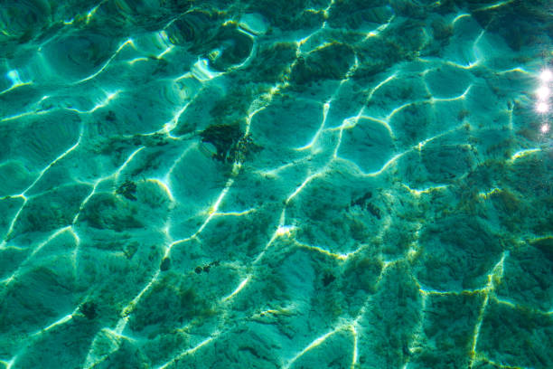 Top view of surface water, sand and rocks under water as background on Peroj beach near Pula in Croatia. Sun reflection from clear water.