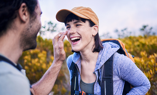Hiking, sunscreen and happy couple on mountain for adventure, holiday and journey in nature. Travel, dating and man and woman laughing with spf cream to explore, trekking and backpacking outdoors