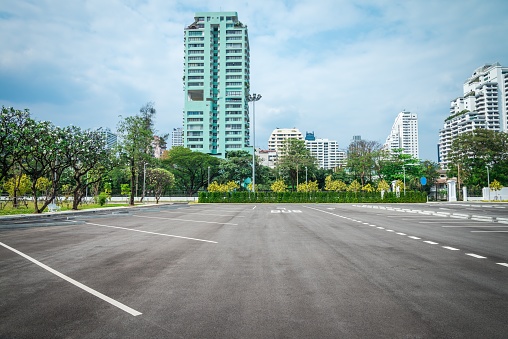 Empty space in outdoors public city park asphalt parking lot area with cityscape background in sunny day. Traffic, transportation, city life concept.