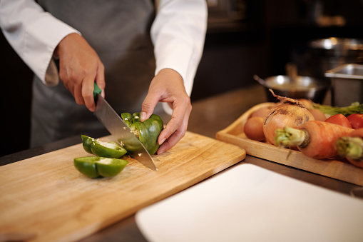 Closeup image of cook cutting green bell pepper with sharp knife when making salad