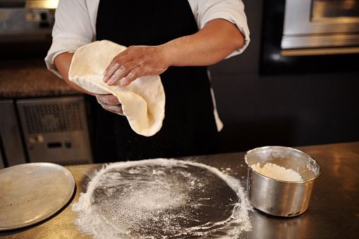 Closeup image of pizza maker putting dough on tray