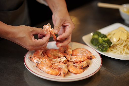 Hands of cook peeling and deveining plate of shrimps