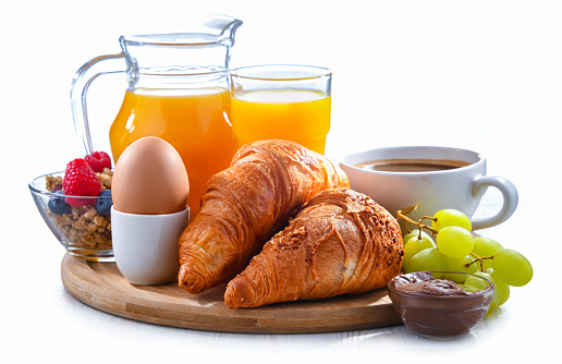 Breakfast served with coffee, orange juice, croissants and egg isolated on white