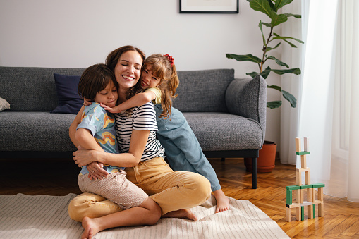 Portrait of a beautiful woman cuddling and hugging with her son and daughter while sitting on the floor. They are all smiling and look happy while being affectionate with each other.