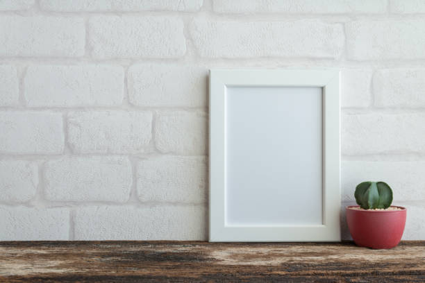 istock White photo frame on old wooden table with succulent pot over white brick wallpaper background. 1616067575