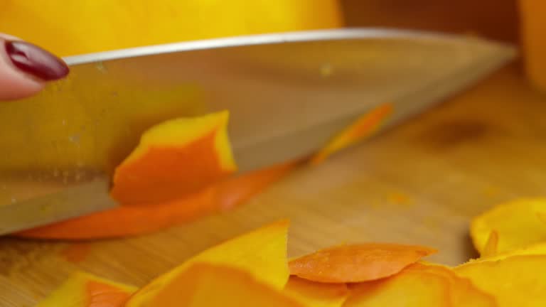 Close-up of hands cuts the peel of a ripe yellow pumpkin on board with a knife