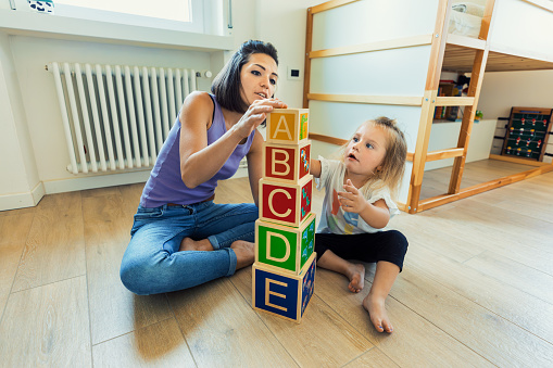 In a room filled with wooden toys, a young woman and her blonde daughter bond, exploring and learning while having fun