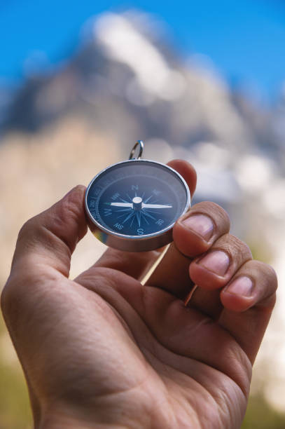 hand of an anonymous person holding a small round compass near a picturesque mountain valley. Blurred background of a snowy mountain on a sunny clear day, vertical photography stock photo