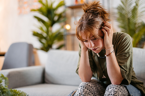 Sad young woman sitting on the sofa at home.