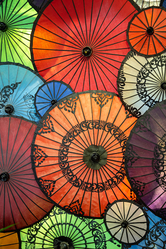 A colorful sunshade umbrella at a popular tourist destination island of Thailand (Khai). In the background you see the azure water and white sand of an idyllic beach. The sky is cloudy, a monsoon rain is approaching.