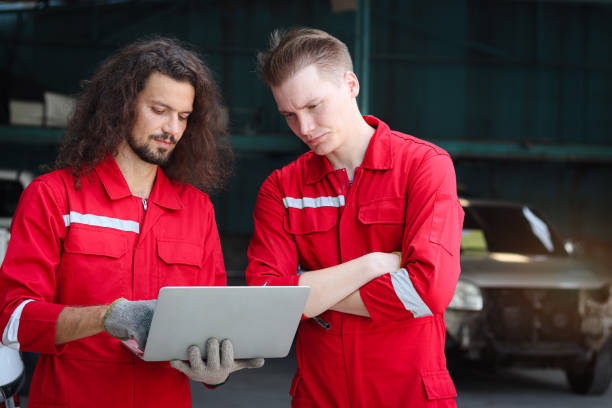 istock Two handsome mechanic men in red uniform holding laptop computer during discussion together at vehicle garage, coworker technician team repairing maintenance customer car automobile at service shop. 1616128462