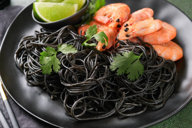 istock Black spaghetti pasta shrimp on black plate on dark concrete table background. Squid ink pasta with prawns. Pasta seafood. Top view on green stone table. Mediterranean traditional cuisine dish. 1616138948