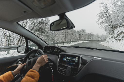 View from the car on the road in a snowy forest, with hands on the steering wheel