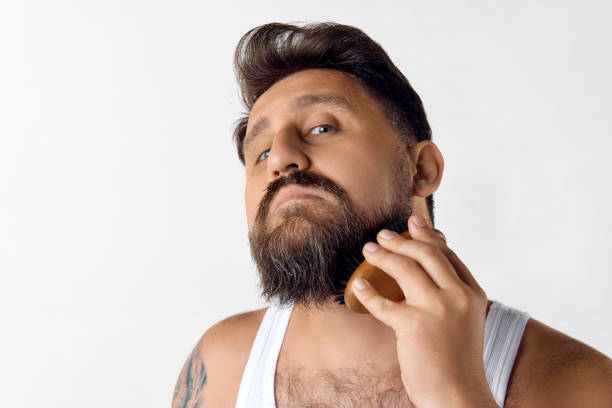istock Mature handsome man taking care after beard with special brush against white studio background. Barbershop 1616148850