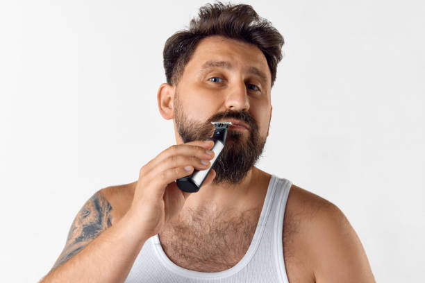 istock Handsome mature man taking care after beard and moustaches with shaver against white studio background. Shaving 1616148863
