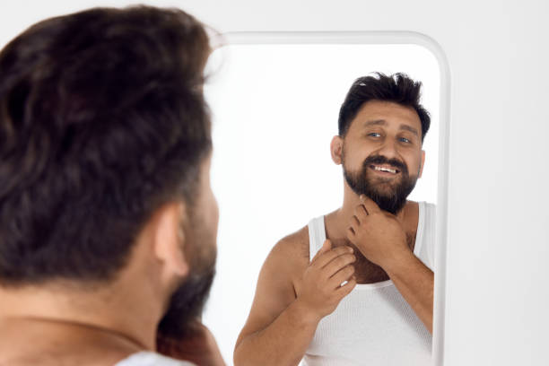 istock Handsome, attractive bearded man in singlet looking in mirror and smiling, taking care after face after shower. Morning routine 1616148880