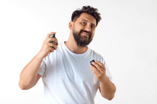istock Handsome, mature, bearded man in white t-shirt applying perfume against white studio background 1616149440