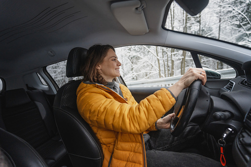 Young happy caucasian woman driving car in winter weather in forest, portrait