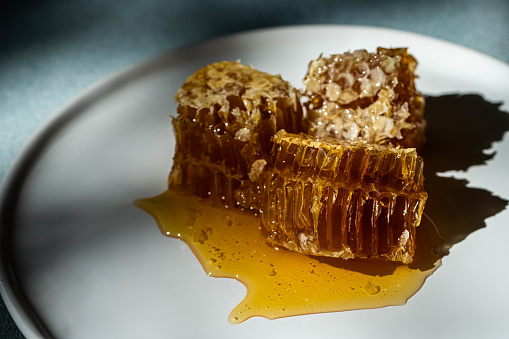 Three pieces of honeycomb with fresh Carpathian honey on white plate.