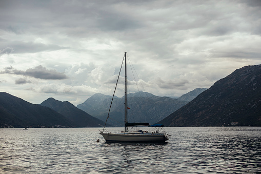 A sailboat in a bay surrounded by mountains with gray clouds in the sky