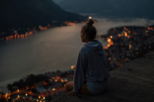 At nightfall, a young woman sits and enjoys the view of a stunning bay