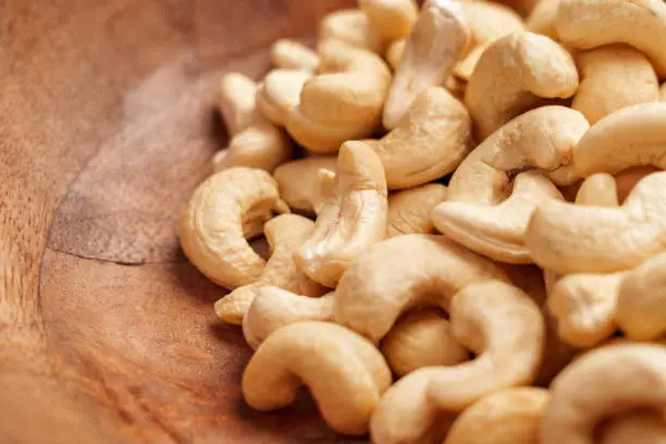 Fresh natural raw cashew nuts in wooden bowl closeup