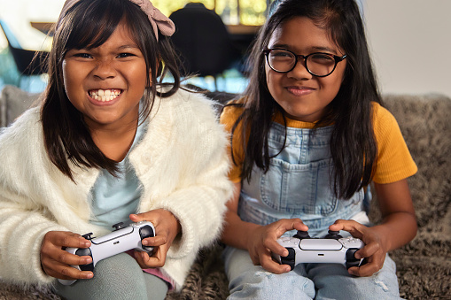 Two excited sisters are immersed in a video game. Their animated expressions and focused gazes reveal their enthusiasm as they share a moment of immersive fun and friendly competition, capturing the dynamic energy and shared excitement that comes with playing a game together.