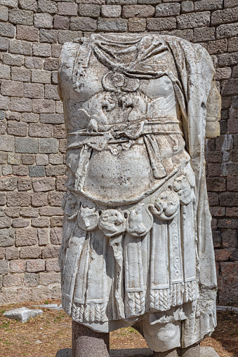 Emperor's armor close-up on an ancient Roman marble statue. Grunge bricks wall background. Vertical shot. Bergama (Ancient Pergamon), Turkey