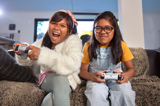 Two excited sisters are immersed in a video game. Their animated expressions and focused gazes reveal their enthusiasm as they share a moment of immersive fun and friendly competition, capturing the dynamic energy and shared excitement that comes with playing a game together.