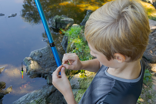 Side view of a young girl standing in the shallow water of a lake as she tries to catch a fish.