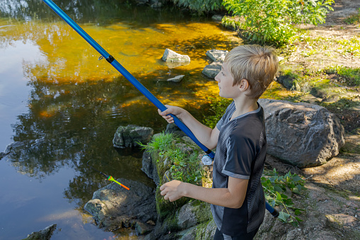 A teenager on a river casts a fishing rod to catch fish. Sport fishing on the river in summer.