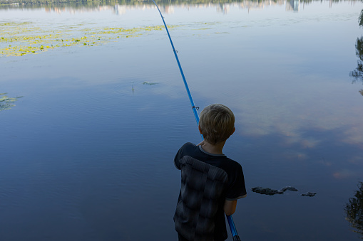 The teenager stands with his back to the rod and waits for a nibble. Sport fishing on the river in summer.
