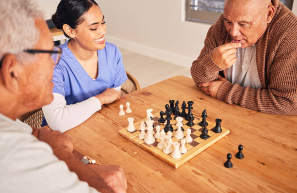 Retirement, playing and chess with senior men at nursing home for fun activity in home with nurse at table. Strategy, chessboard and challenge with elderly friends together on table for bonding.