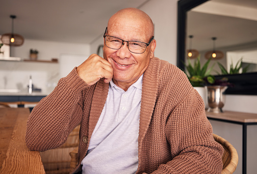 Portrait, smile and glasses with a senior man sitting in the living room of his home during old age retirement. Relax, wrinkles and satisfaction with a happy elderly male pensioner in his house