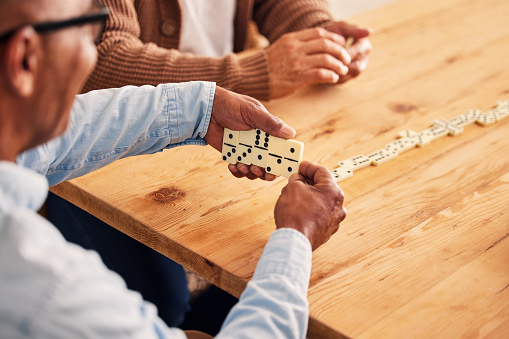 Hands, dominoes and a senior man playing a game at a table in the living room of a retirement home. Thinking, strategy and fun with an elderly male pensioner in a house closeup for entertainment
