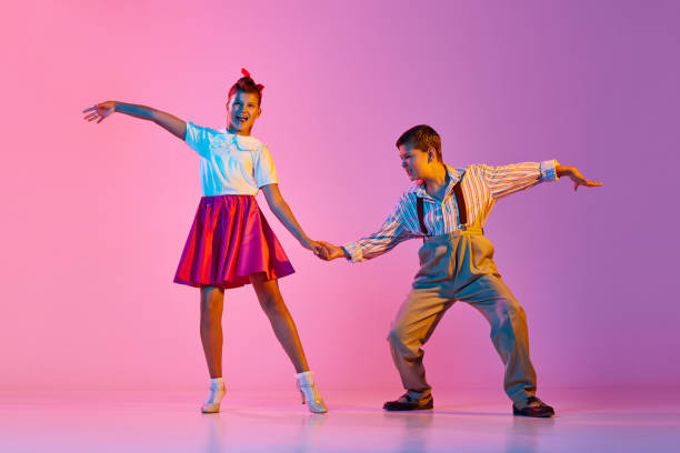 Talented, artisitc children, boy and girl in retro clothes dancing lindy hop against pink studio background in neon light Talented, artisitc children, boy and girl in retro clothes dancing lindy hop against pink studio background in neon light. Concept of childhood, hobby, active lifestyle, performance, art, fashion rockabilly boys stock pictures, royalty-free photos & images