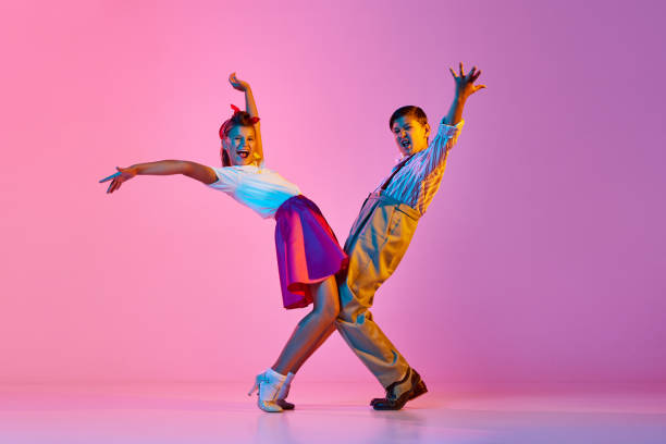 Talented, artisitc children, boy and girl in retro clothes dancing lindy hop against pink studio background in neon light Talented, artisitc children, boy and girl in retro clothes dancing lindy hop against pink studio background in neon light. Concept of childhood, hobby, active lifestyle, performance, art, fashion rockabilly boys stock pictures, royalty-free photos & images