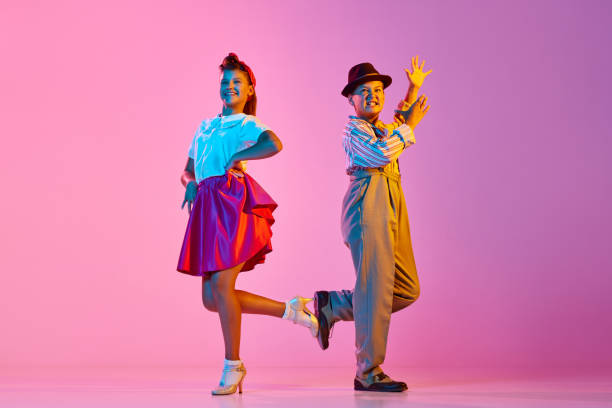 Emotional, beautiful children, boy and girl in retro costumes dancing lindy hop against pink studio background in neon light Emotional, beautiful children, boy and girl in retro costumes dancing lindy hop against pink studio background in neon light. Concept of childhood, hobby, active lifestyle, performance, art, fashion rockabilly boys stock pictures, royalty-free photos & images