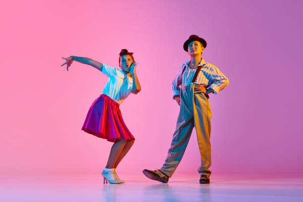 Emotional, beautiful children, boy and girl in retro costumes dancing lindy hop against pink studio background in neon light Emotional, beautiful children, boy and girl in retro costumes dancing lindy hop against pink studio background in neon light. Concept of childhood, hobby, active lifestyle, performance, art, fashion rockabilly boys stock pictures, royalty-free photos & images