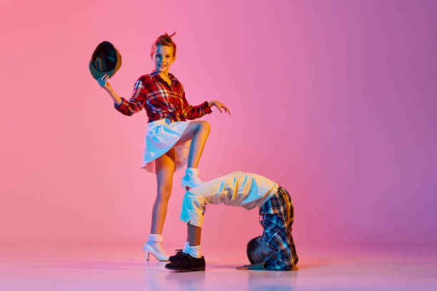 Flexibility. Stylish, active children, girl and boy in retro style clothes dancing against pink studio background in neon light Flexibility. Stylish, active children, girl and boy in retro style clothes dancing over pink studio background in neon light. Concept of childhood, hobby, active lifestyle, performance, art, fashion rockabilly boys stock pictures, royalty-free photos & images