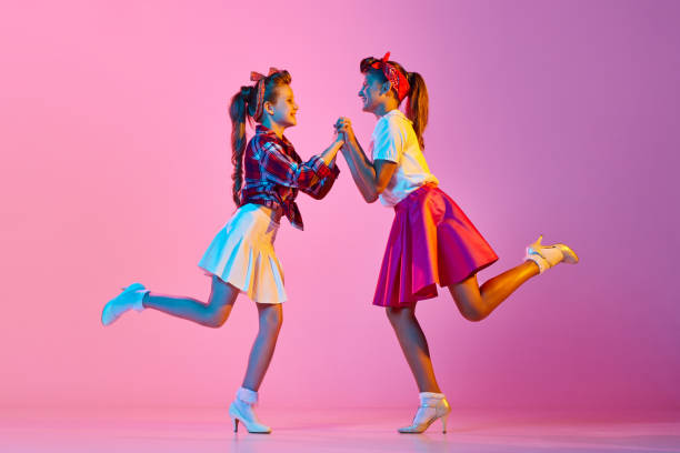 Beautiful, stylish girls, children in retro clothes dancing lindy hop against pink studio background in neon light Beautiful, stylish girls, children in retro clothes dancing lindy hop against pink studio background in neon light. Concept of childhood, hobby, active lifestyle, performance, art, fashion rockabilly boys stock pictures, royalty-free photos & images