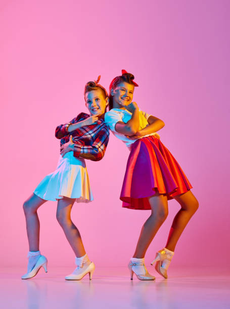 Beautiful, stylish girls, children in retro clothes dancing lindy hop against pink studio background in neon light Beautiful, stylish girls, children in retro clothes dancing lindy hop against pink studio background in neon light. Concept of childhood, hobby, active lifestyle, performance, art, fashion rockabilly boys stock pictures, royalty-free photos & images