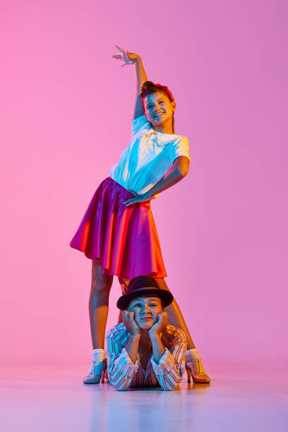 Emotive, stylish children,. boy and girl in beautiful clothes dancing retro dance against pink studio background in neon light Emotive, stylish children,. boy and girl in beautiful clothes dancing retro dance against pink studio background in neon light. Concept of childhood, hobby, active lifestyle, performance, art, fashion rockabilly boys stock pictures, royalty-free photos & images