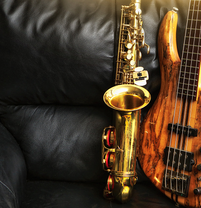 Alto sax and bass guitar standing up on an armchair made of black leather. Plenty of copy space.