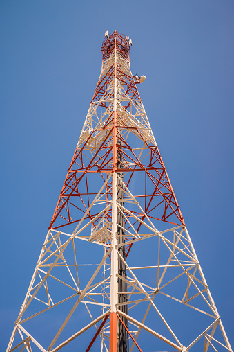 Red white telecommunication tower against blue sky background. Technology communication, internet, mobile network concept.