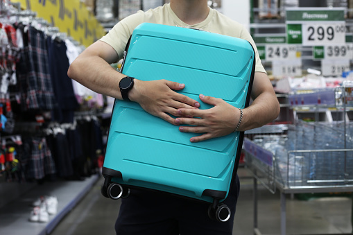 Hands of a man holding a heavy travel suitcase in a store. Choosing a suitcase on wheels for things before traveling